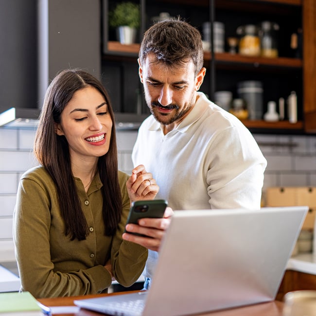 couple-checking-home-finances-on-smartphone-and-laptop